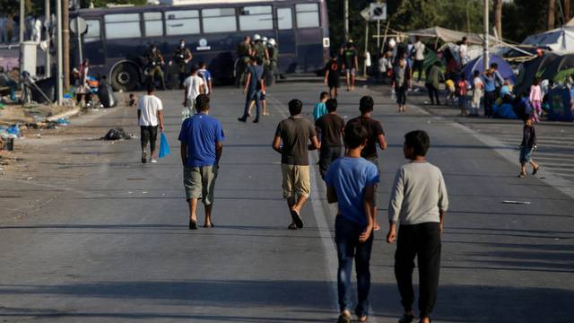 Refugees and migrants from the destroyed Moria camp make their way on a road blocked by police, during an operation to move them to a new temporary camp, on the island of Lesbos