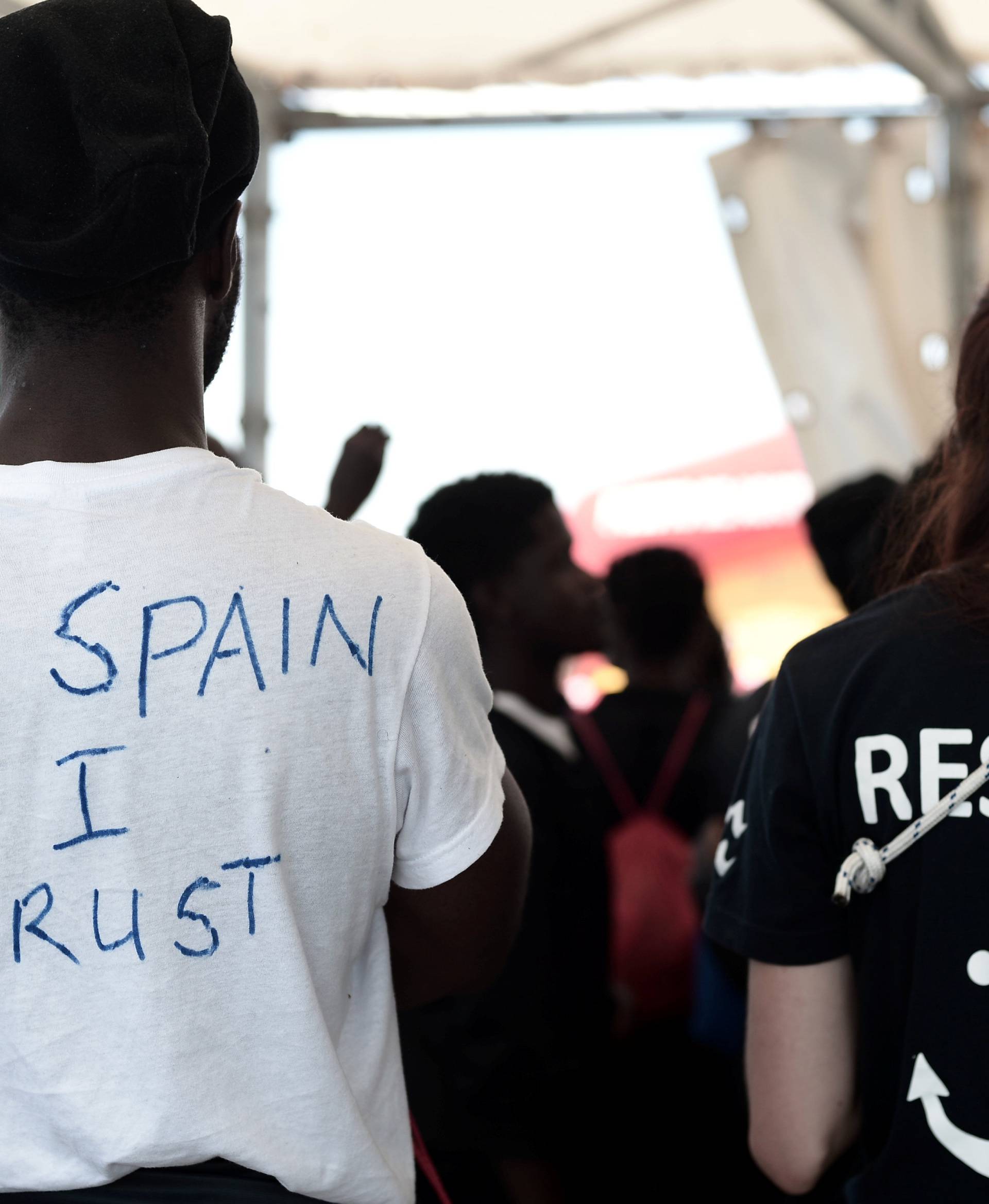 A migrant wearing a t-shirt reading "In Spain I Trust" waits to disembark from the Aquarius rescue ship at port in Valencia