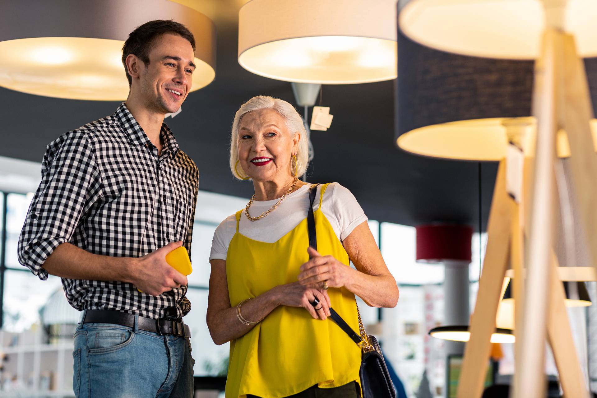 Beaming gorgeous senior lady discussing lamps buying with younger beau