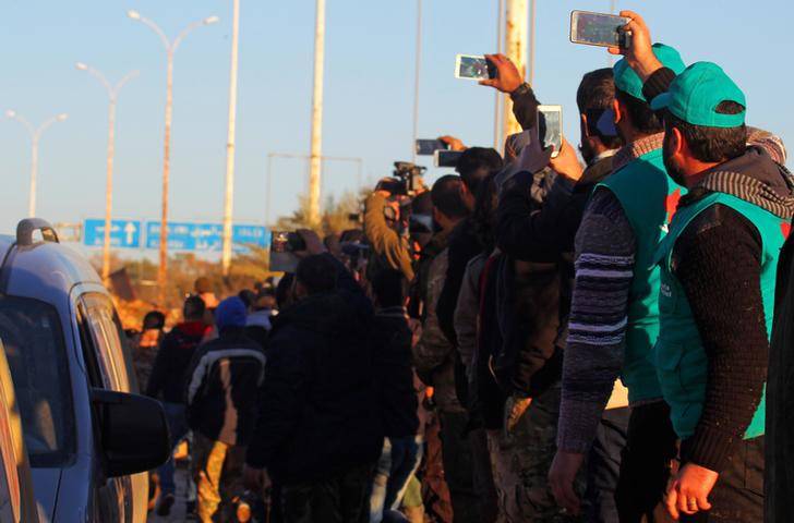 Rebel fighters and civilians take pictures of the convoy of evacuees from rebel-held east Aleppo, upon their arrival to the town of al-Rashideen, which is held by insurgents