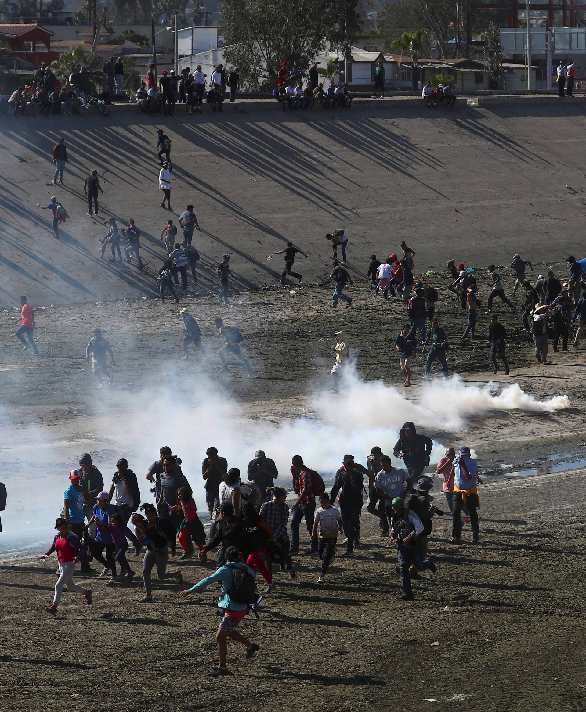 Migrants run from tear gas thrown by the U.S border patrol near the fence between Mexico and the United States in Tijuana