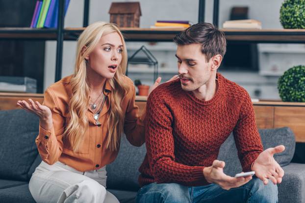 emotional upset couple sitting on couch and quarreling about smartphone, mistrust concept