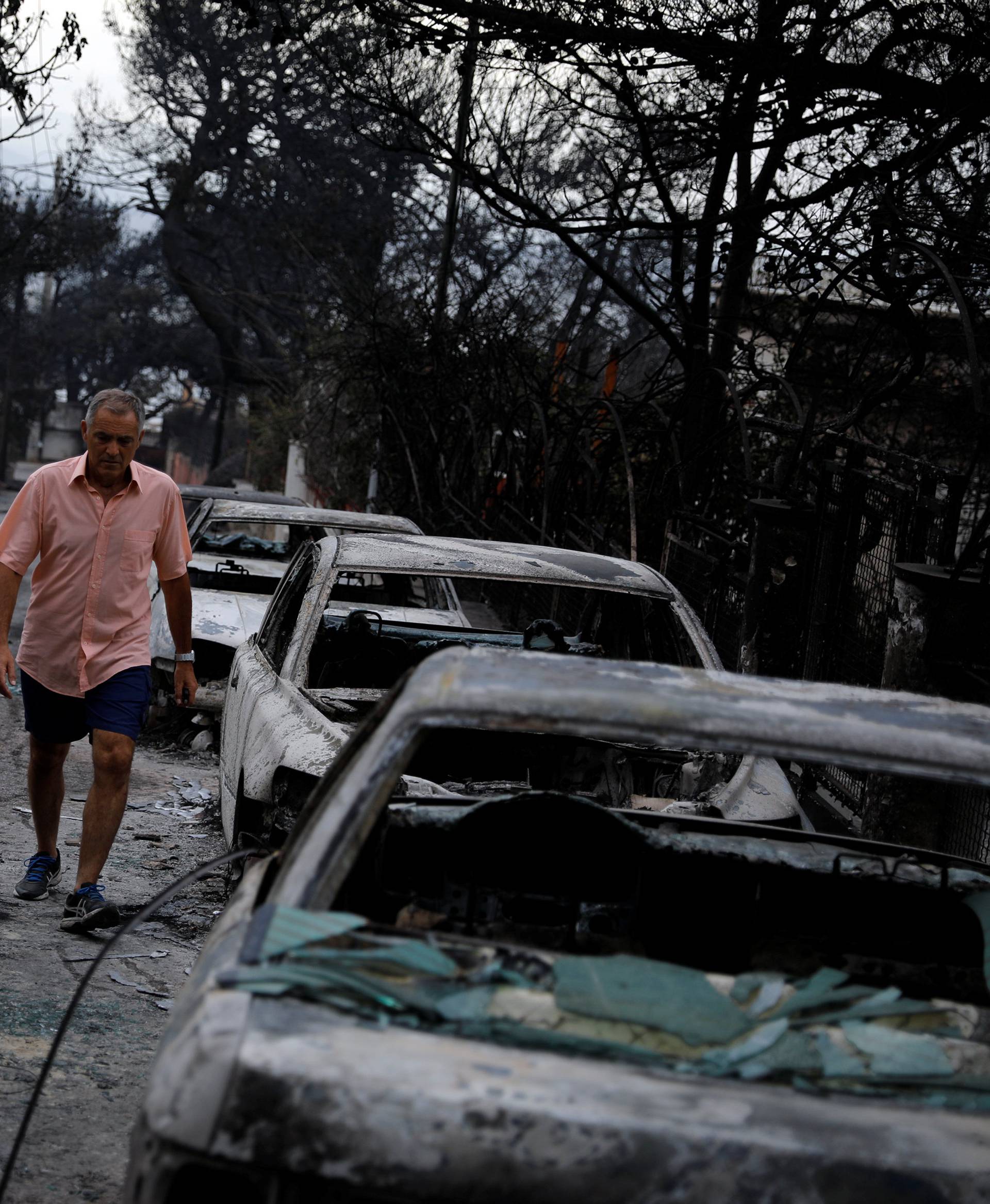 A man walks among burnt cars following a wildfire at the village of Mati