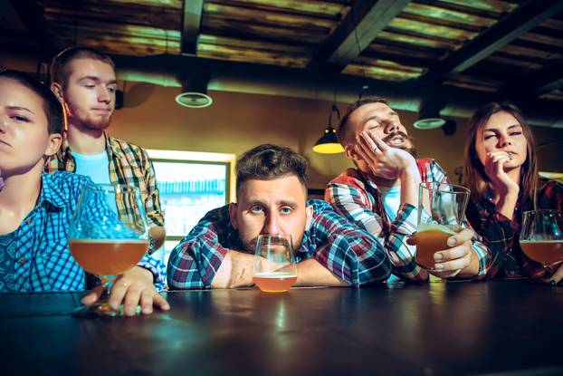 Upset male and female friends watching sport game or football match and drinking beer at bar or pub.