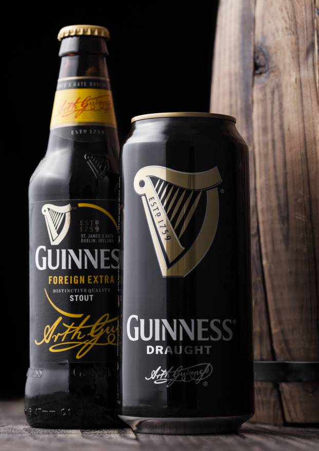 LONDON, UK - MAY 03, 2018: Aluminium can and glass bottle of Guinness draught stout beer next to wooden barrel on dark wooden background.