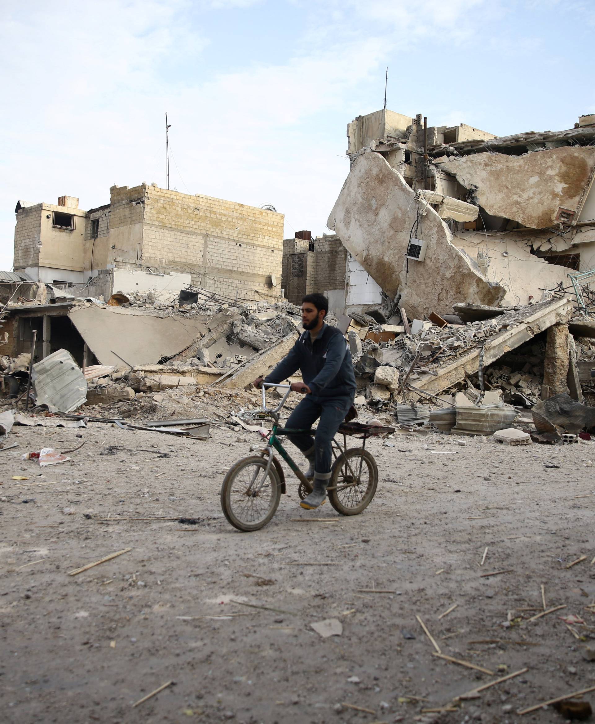 A young man rides bicycle near damaged houses in the besieged town of Douma