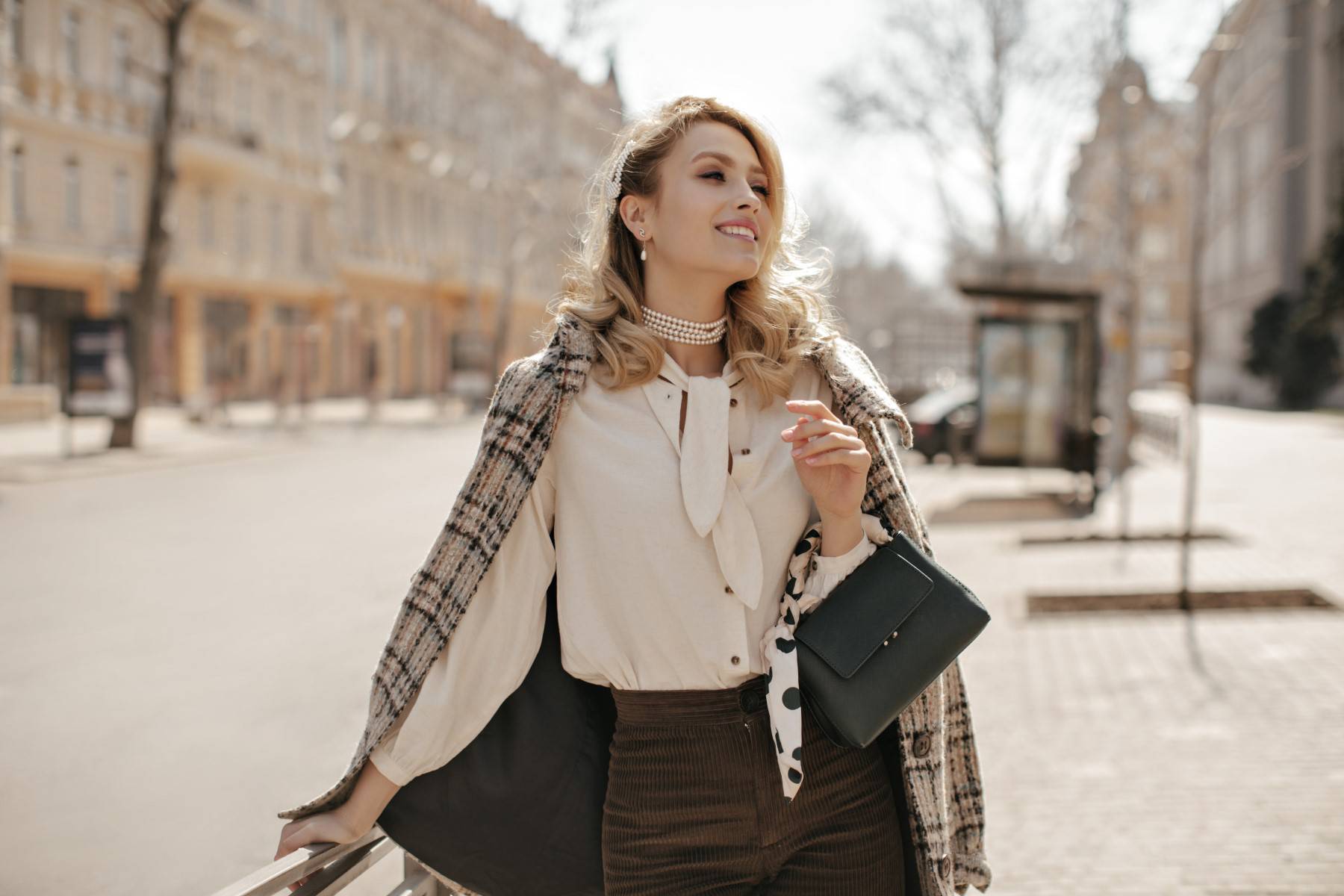 Attractive curly blonde woman in checkered tweed coat, white blouse and brown pants smiles sincerel