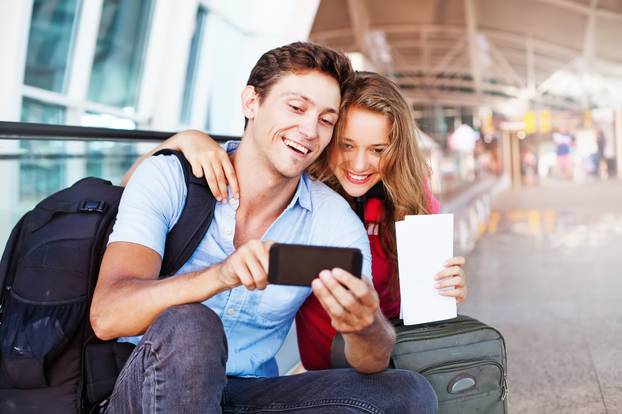 Couple,In,Airport,Using,Travel,App,On,Smart,Phone