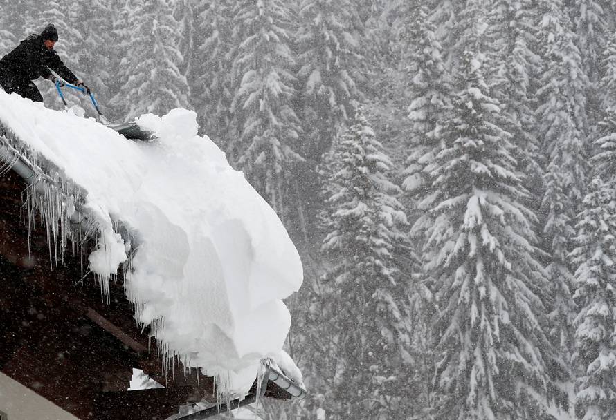 A man shovels snow on a rooftop during heavy snowfall in Filzmoos