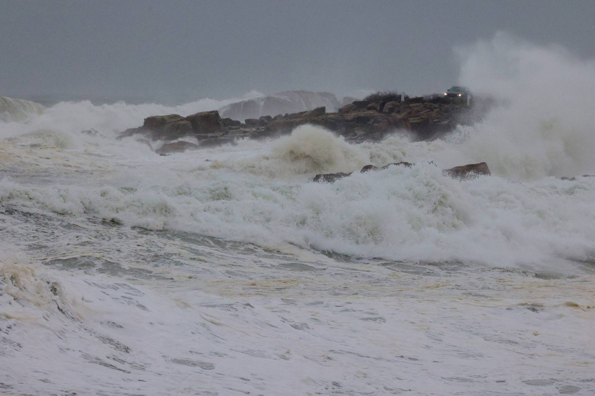 A driver watches the crashing waves at high tide during a winter storm in Gloucester