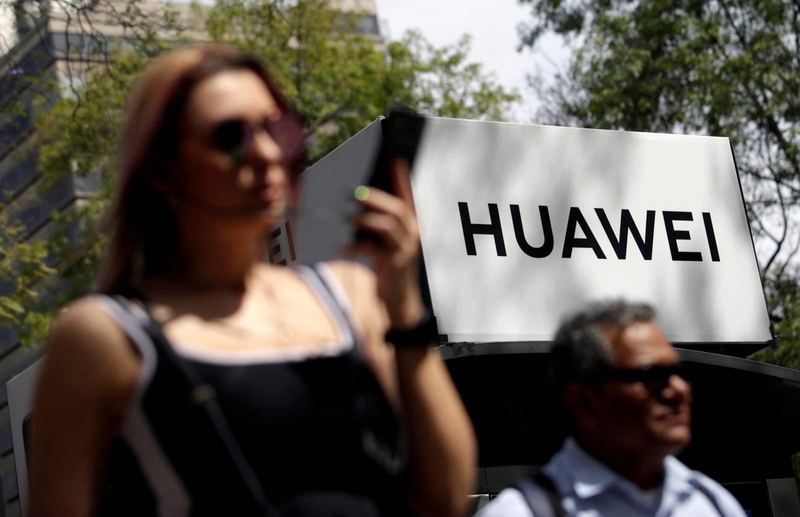 FILE PHOTO: People walk past a Huawei company logo at a bus stop in Mexico City