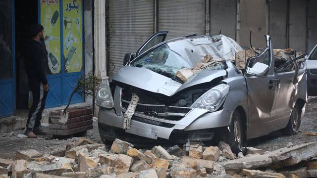 A man stands near a damaged vehicle, following an earthquake, in rebel-held Azaz