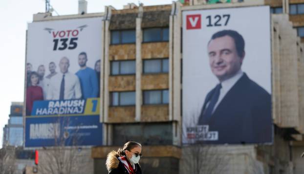 Woman wearing a mask walks near electoral campaign billboards in Pristina