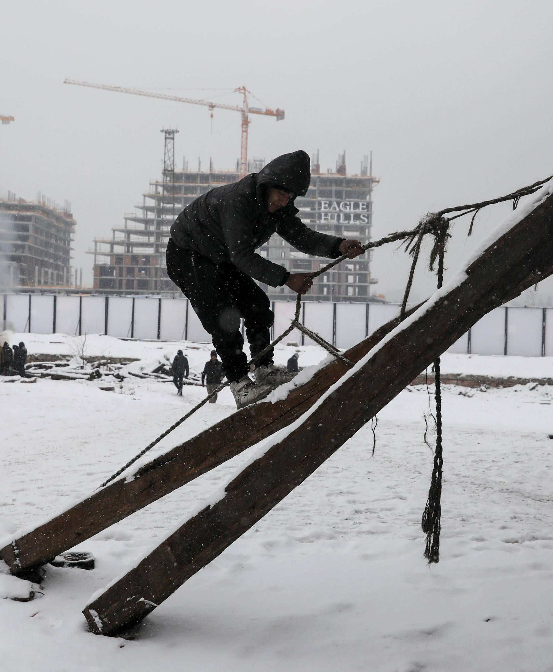 A migrant climbs during a snowfall outside a derelict customs warehouse in Belgrade