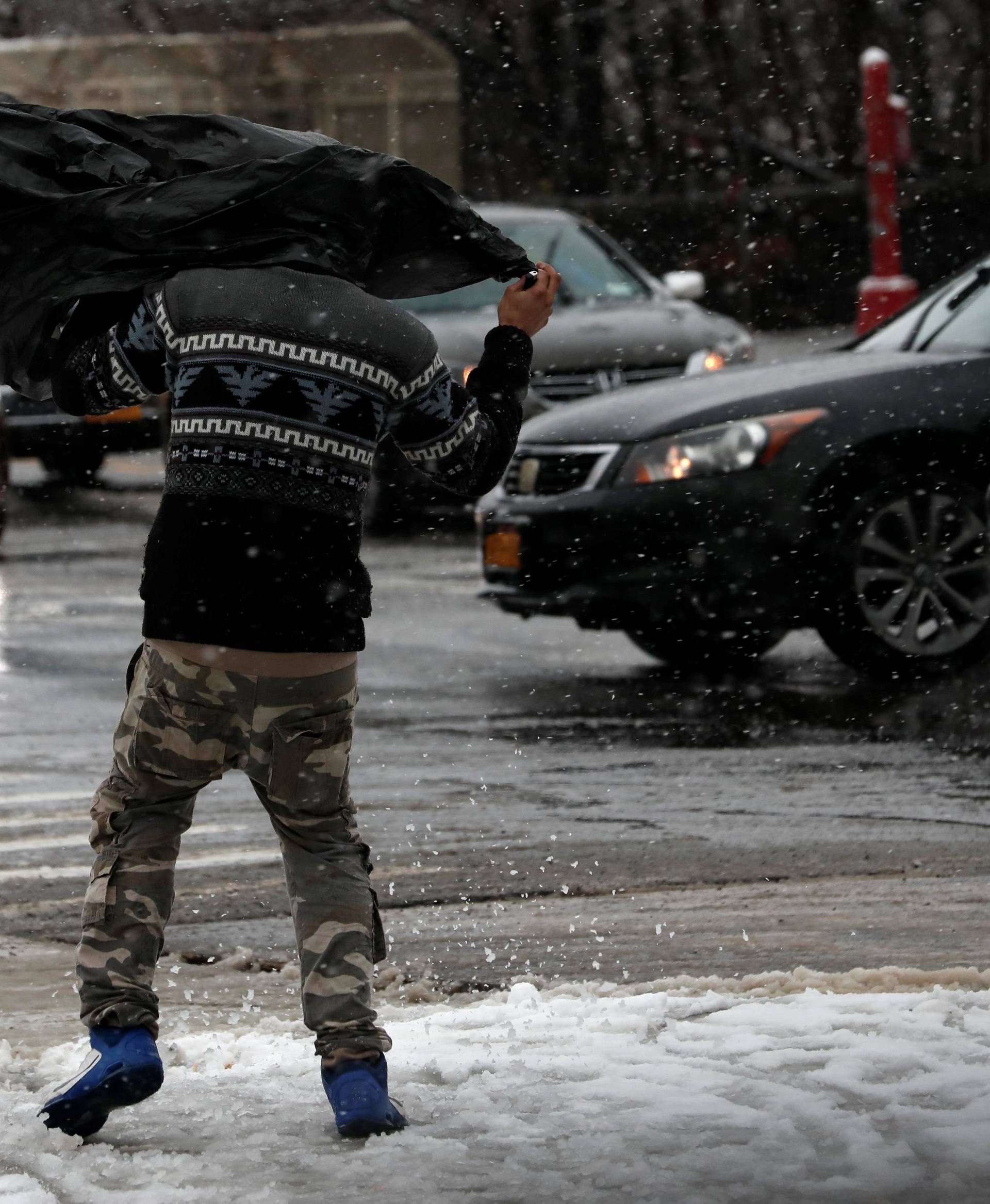 A man struggles in the wind beneath a plastic bag as he walks during a snowstorm in upper Manhattan in New York City