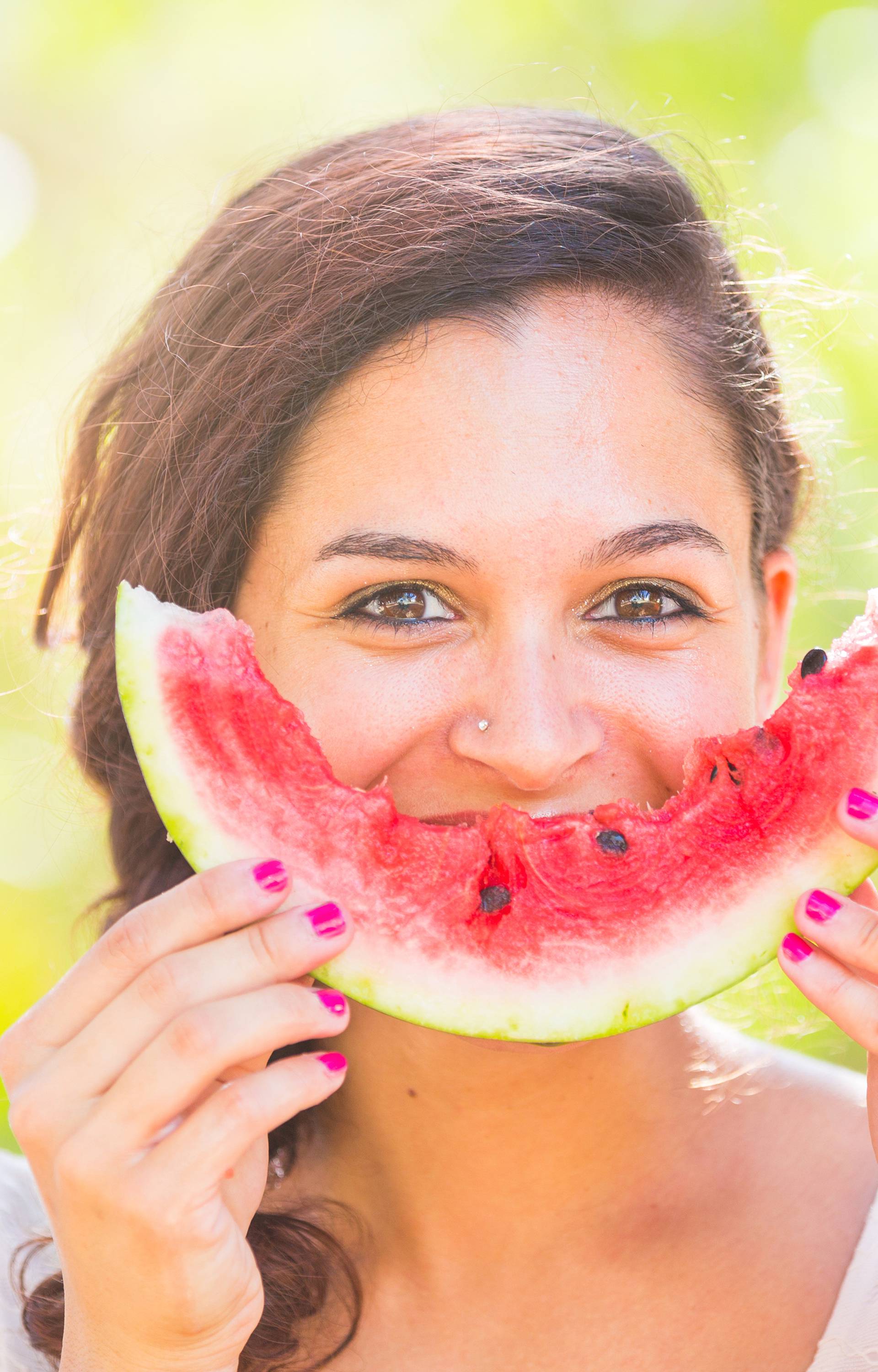 Beautiful young woman at park eating a slice of watermelon