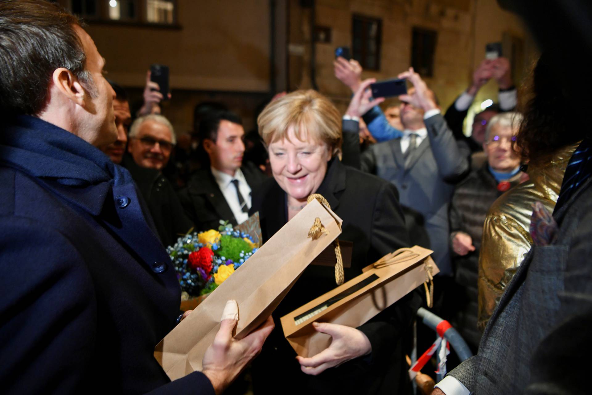 Outgoing German Chancellor Angela Merkel and France's President Emmanuel Macron receive flowers and a bottle of wine as gifts upon their arrival for talks, in Beaune