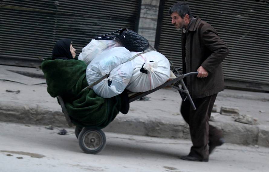 A man pushes a cart carrying an elderly woman and belongings as they flee deeper into the remaining rebel-held areas of Aleppo