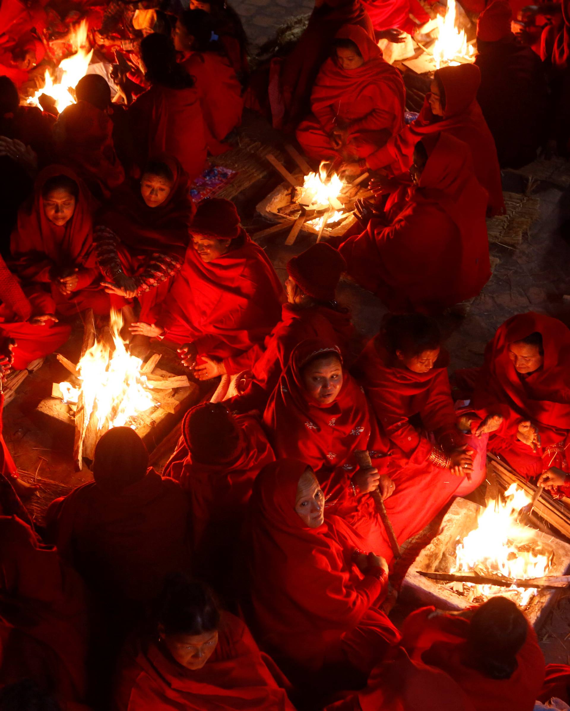 Hindu women sit around fires to keep warm before taking holy baths at Saali River during the Swasthani Brata Katha festival at Sankhu in Kathmandu