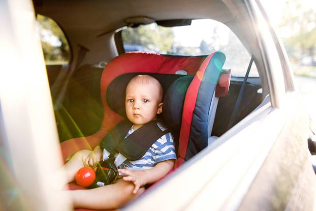Little baby boy sitting in the car seat in the car.