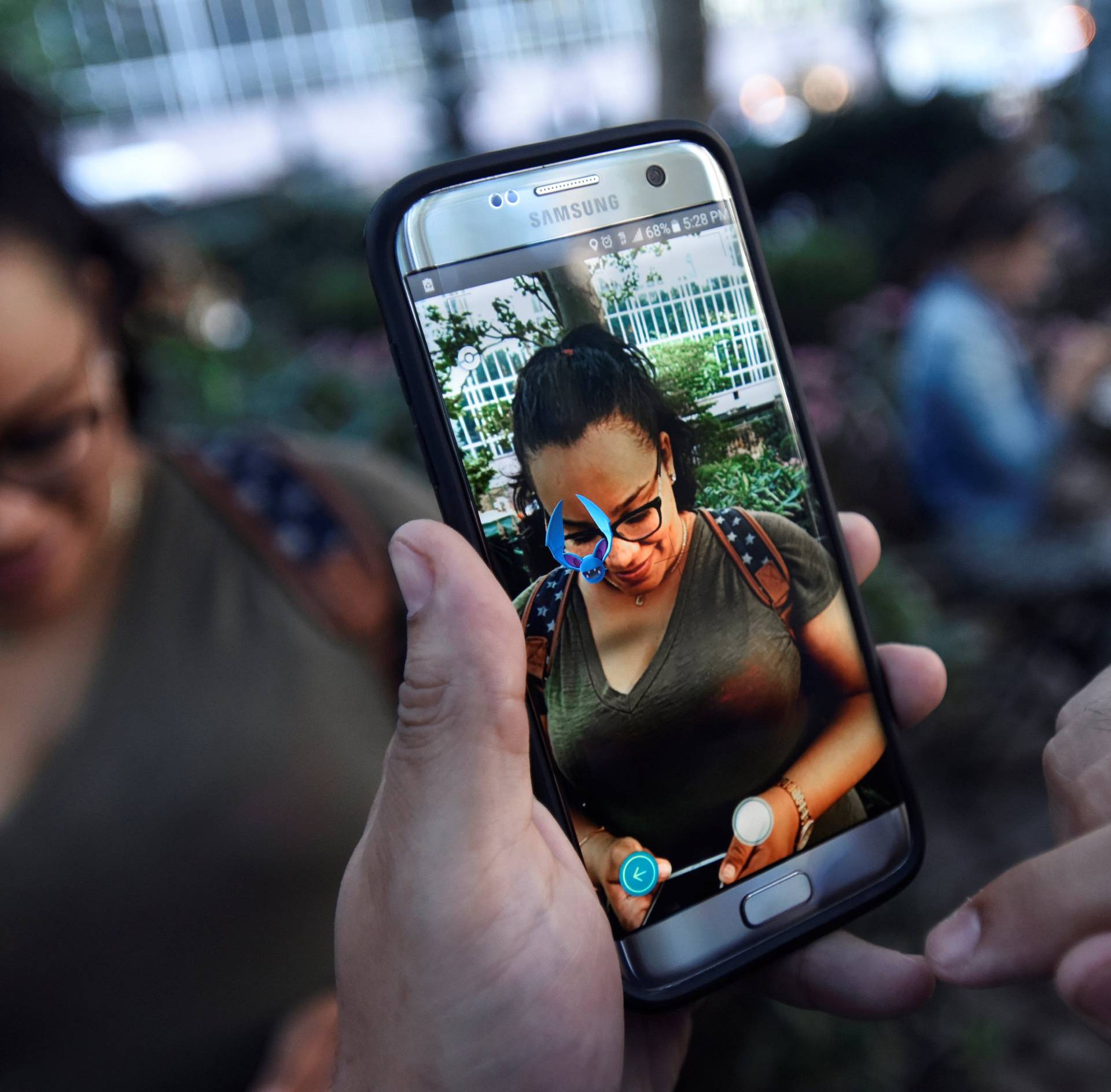 A Pokemon appears on the screen next to a woman as a man plays the augmented reality mobile game "Pokemon Go" by Nintendo in Bryant Park in New York City