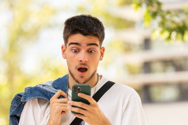 young man in the street looking at the phone with a surprised expression