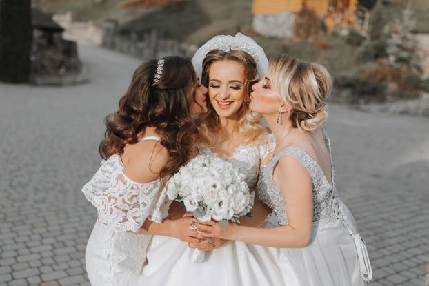 Stylish bridesmaids have fun with the bride in nature and pose and kiss the bride
