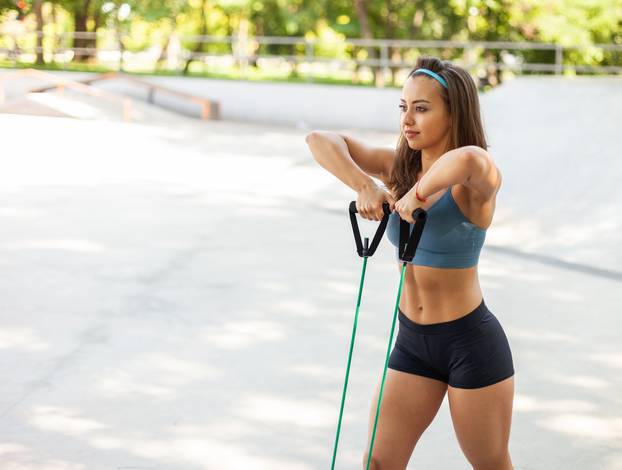 Young athletic woman exercising with a rubber expander outdoors. Healthy lifestyle