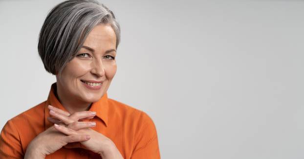 Happy aged woman smiling fingers crossed. Lady with bob hairstyle in orange blouse, head and shoulders portrait. Wisdom concept. Horizontal blank or template with copy spase at right side