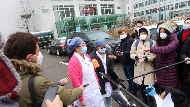 Medical workers wearing face masks speak to journalists outside a hospital where three patients cured of the novel coronavirus were discharged, in Beijing