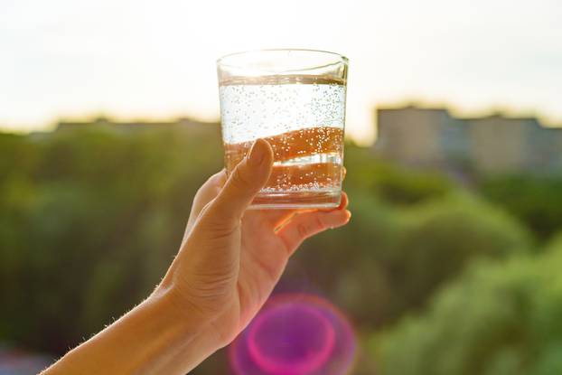 Glass of clear, ecology water in hand. Background sky, silhouette of the city, sunset