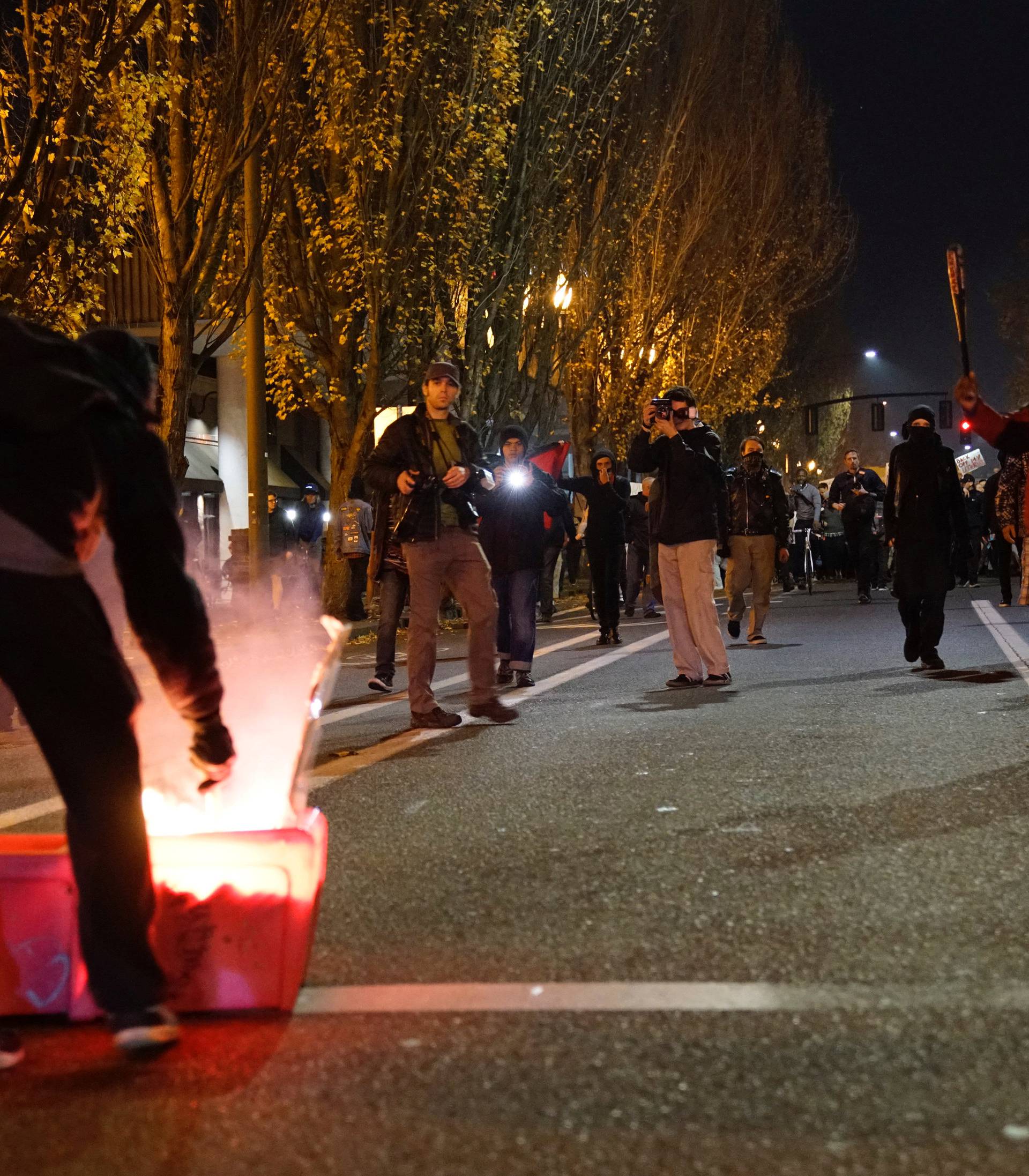 A demonstrator sets a news rack on fire as another wields a baseball bat during a protest against the election of Republican Donald Trump as President of the United States in Portland