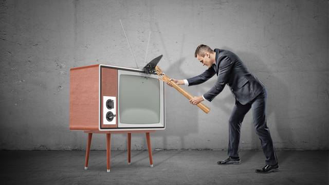 A businessman on concrete background fails to smash an old retro TV set with a broken hammer.