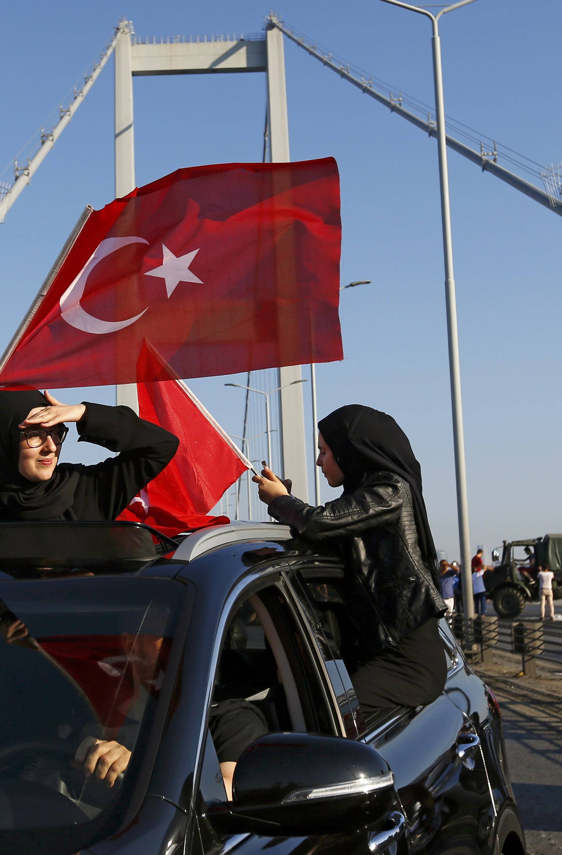 Women wave Turkish flags after troops involved in the coup surrendered on the Bosphorus Bridge in Istanbul