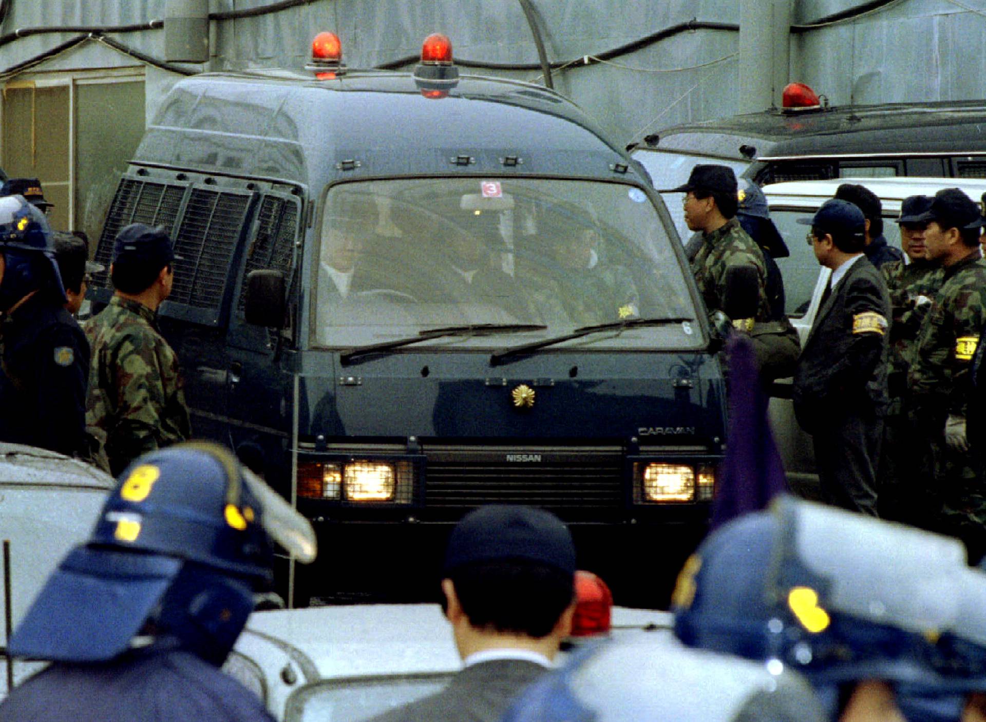 FILE PHOTO : A police vehicle transporting Aum Shinri Kyo sect guru Shoko Asahara is surrounded by policemen as the doomsday prophet is arrested at the cult's Kamikuishiki compounds