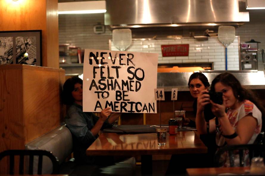 Patrons hold a sign as people march by while protesting the election of Republican Donald Trump as the president of the United States in downtown Los Angeles