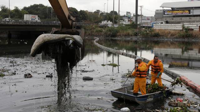 Men work cleaning up the garbage next to an ecobarrier at Meriti River which flows into Guanabara Bay, in Duque de Caxias, near Rio de Janeiro