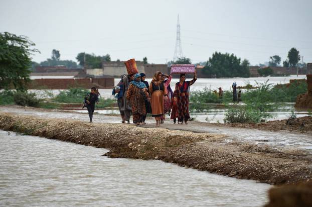 Women and children walk with their belongings towards a higher ground following rains and floods during the monsoon season in Dera Allah Yar,