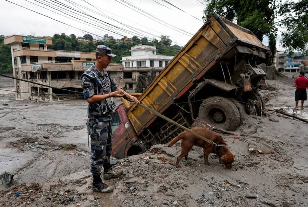 A security force member and his sniffer dog search for survivors following devastating floods, in Trishuli
