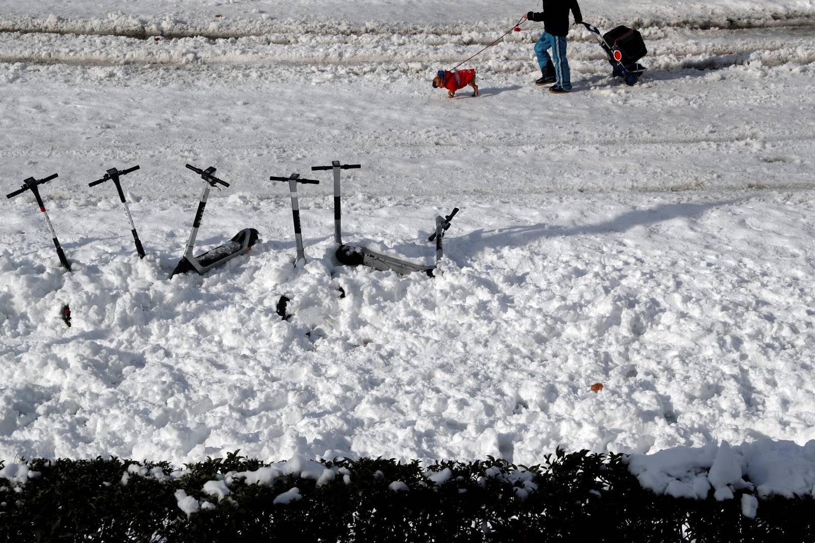 A man walks past scooters buried in snow, in Madrid