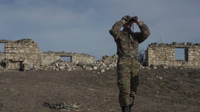 FILE PHOTO: An ethnic Armenian soldier looks through binoculars as he stands at fighting positions near divided Taghavard village in Nagorno-Karabakh region