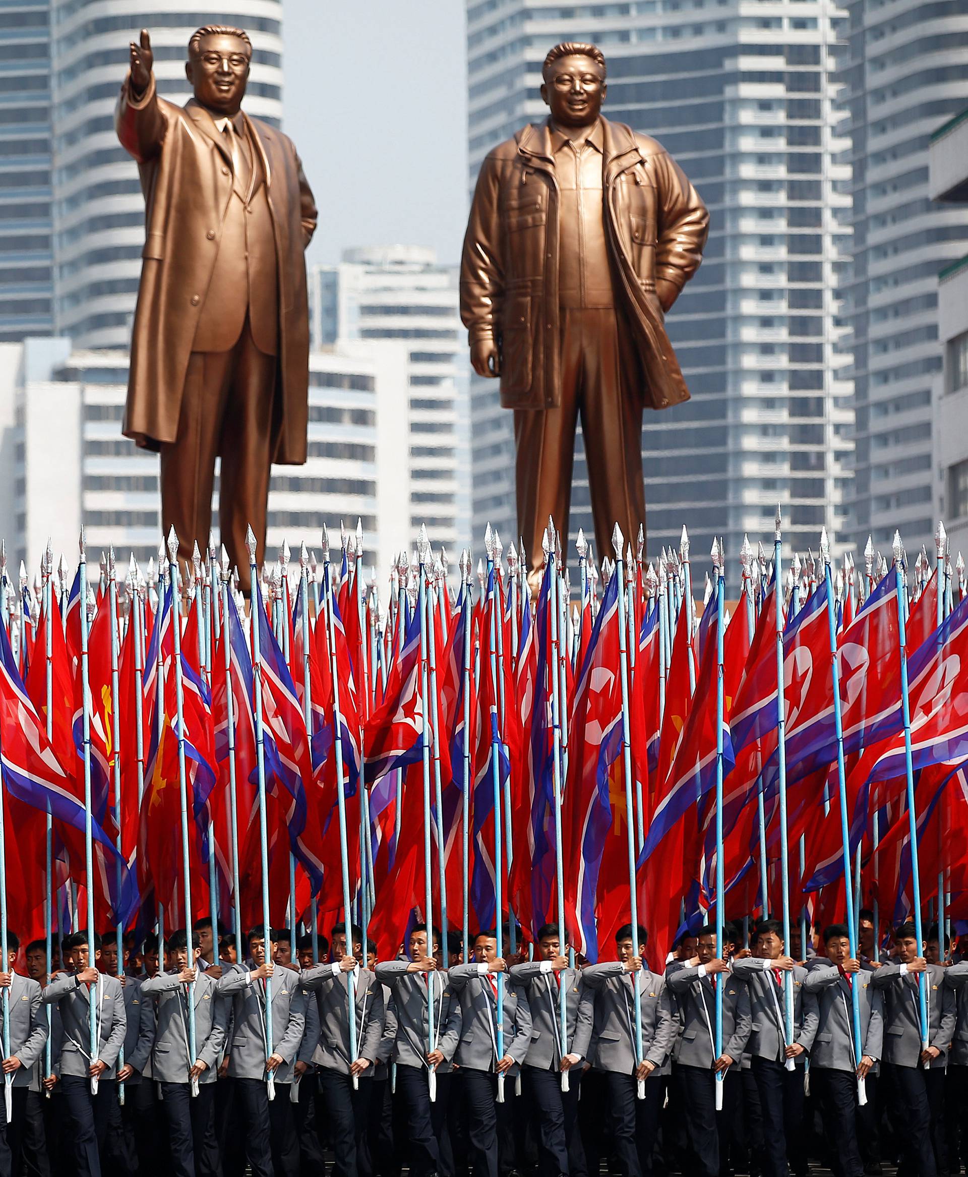 People carry flags in front of statues of North Korea founder Kim Il Sung and late leader Kim Jong Il during a military parade marking the 105th birth anniversary Kim Il Sung in Pyongyang