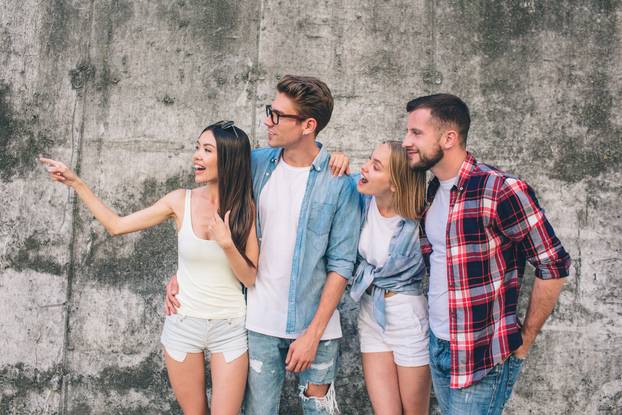 A Picture of Chinese Girl Looking to the Left. Also she is pointing to that side. Her friends are standing very close to her and looking at the Same Direction. Standing on Gray Background.