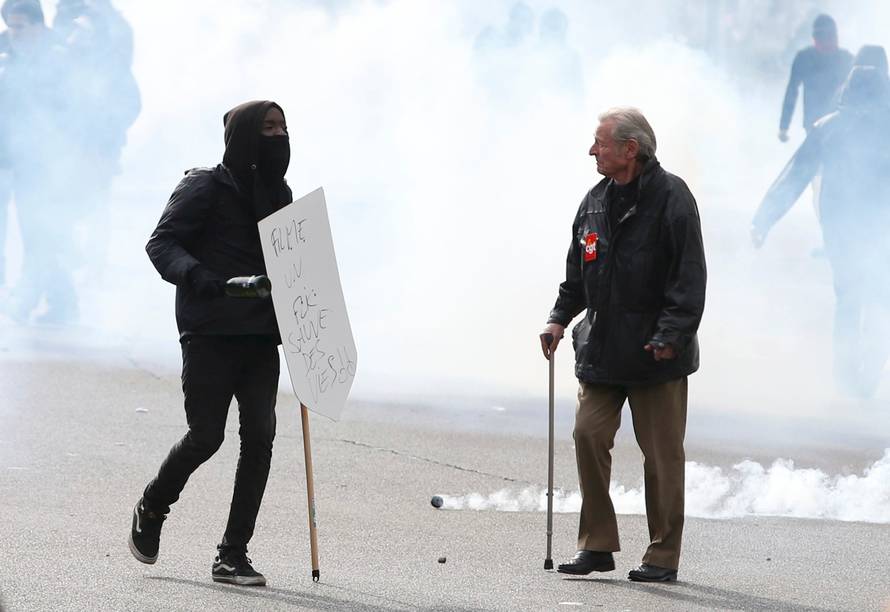 A masked youth and a demonstrator walk through a cloud of tear gas during a demonstration against the French labour law proposal in Paris