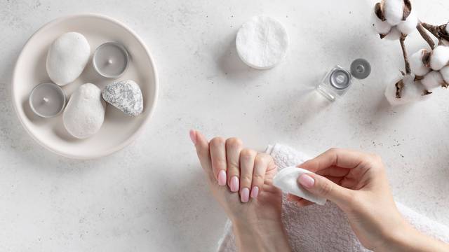 young woman removing pink nail polish with remover liquid. Personal hygiene and care concept. White concrete background, flat lay.