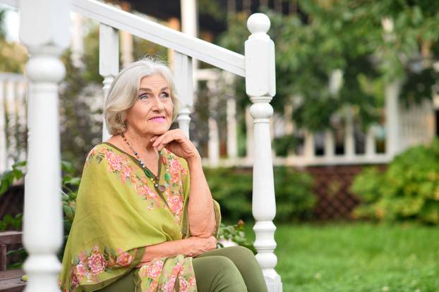 Elderly woman sitting in the yard of her house
