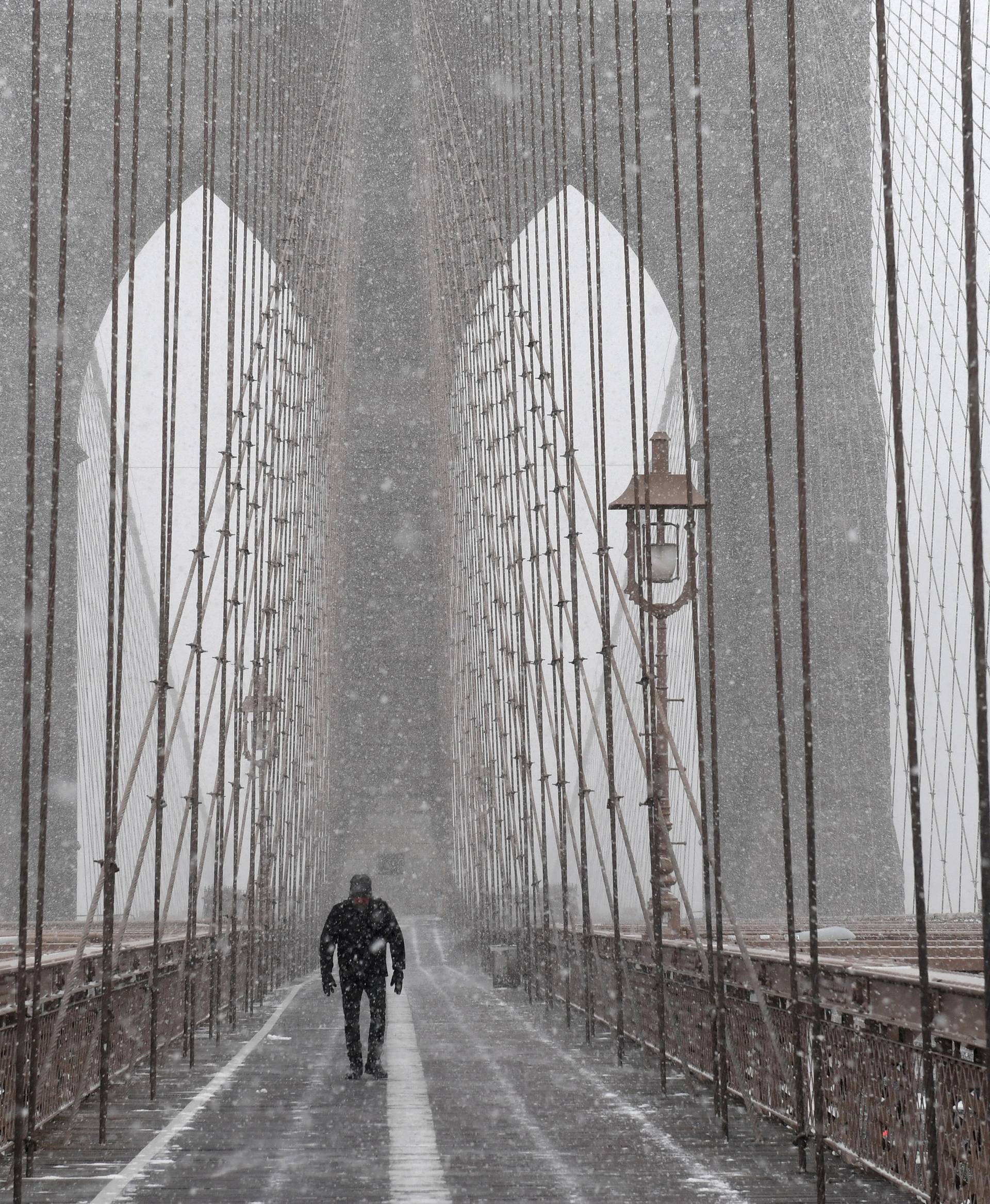 A pedestrian walks through blinding snow across the Brooklyn Bridge during Storm Grayson in New York City