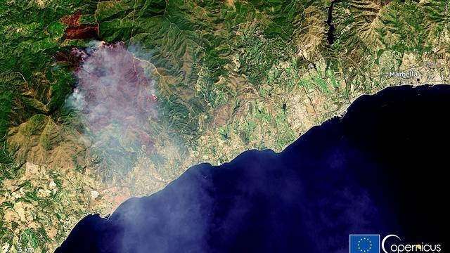 A burning area can be seen in a forested mountain range above Estepona