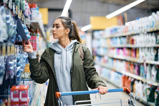Young,Woman,Shopping,Supplies,In,Supermarket,And,Looking,At,Product