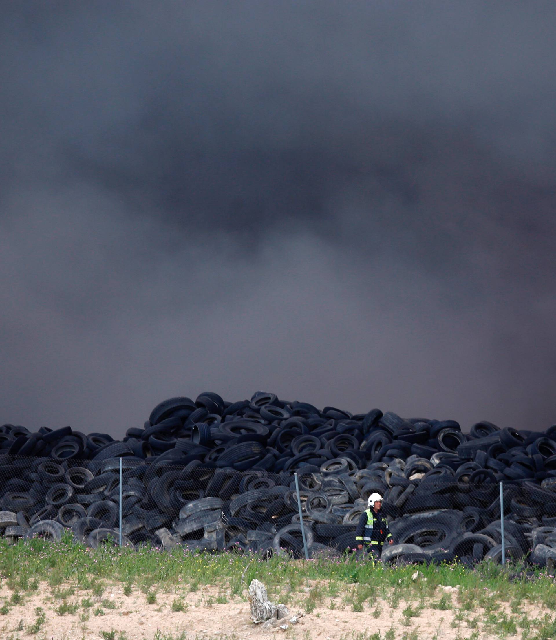 A firefigther walks amidst smoke during a fire at a tire dump near a residential development in Sesena